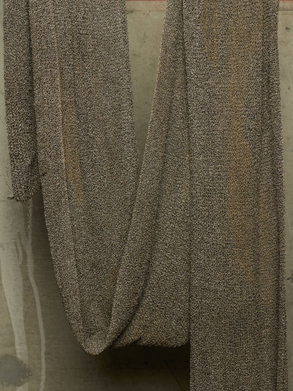A close-up of draped textured fabric in a speckled taupe and brown pattern, hanging against a neutral concrete-like background.