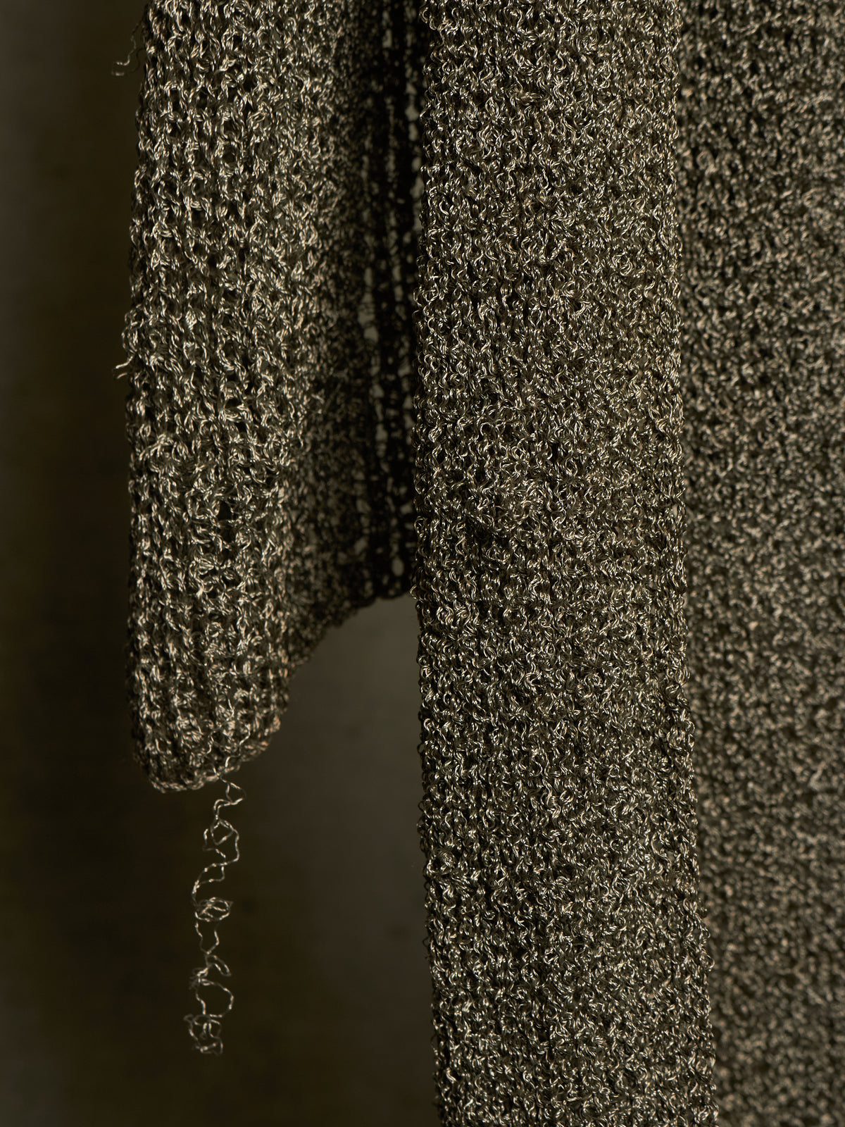 Close-up of a dark metallic textured knit fabric, showing a ribbed sleeve and body with a shimmering bronze and black finish.