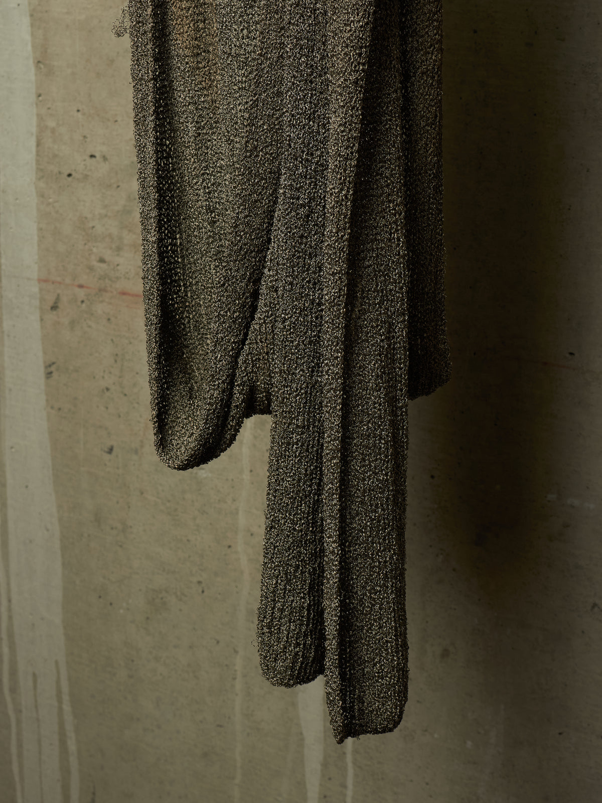 A dark brown textured knit sweater draped against a concrete wall.