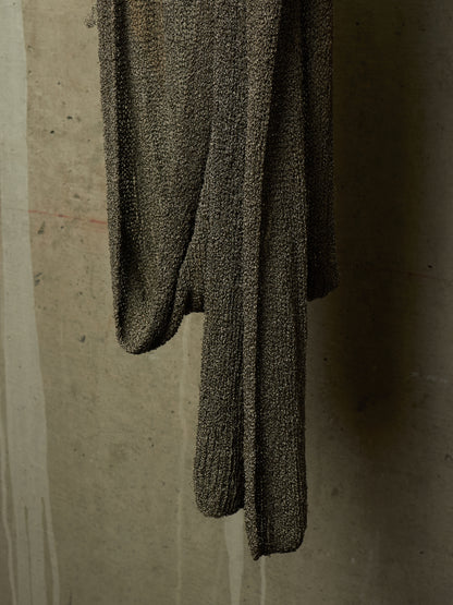 A dark brown textured knit sweater draped against a concrete wall.