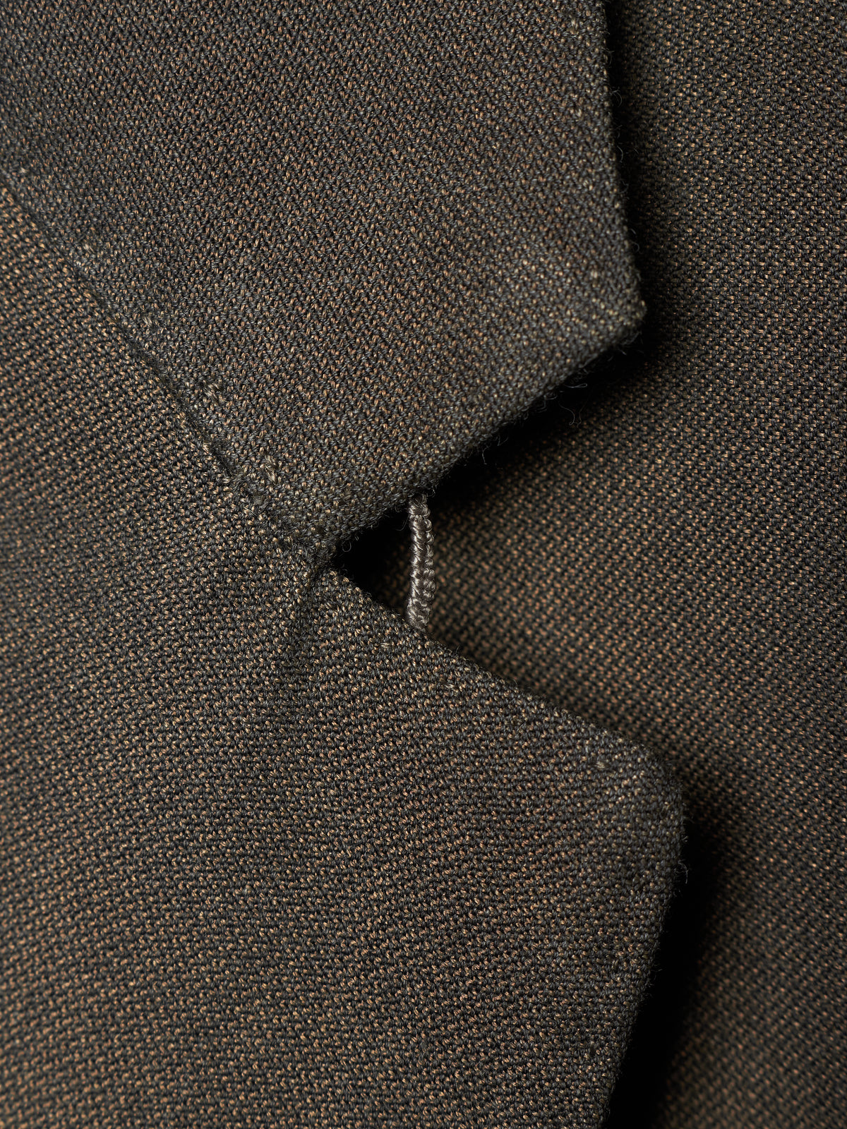 Close-up detail of a dark brown textured fabric garment, showing a folded collar or lapel with fine woven texture and a small stitched tab detail.