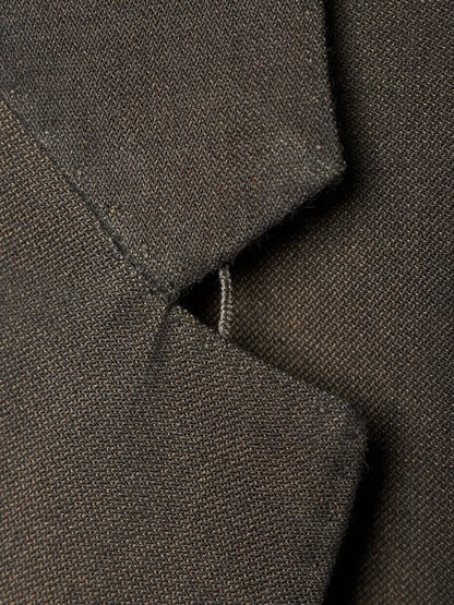 Close-up detail of a dark brown textured fabric garment, showing a folded collar or lapel with fine woven texture and a small stitched tab detail.