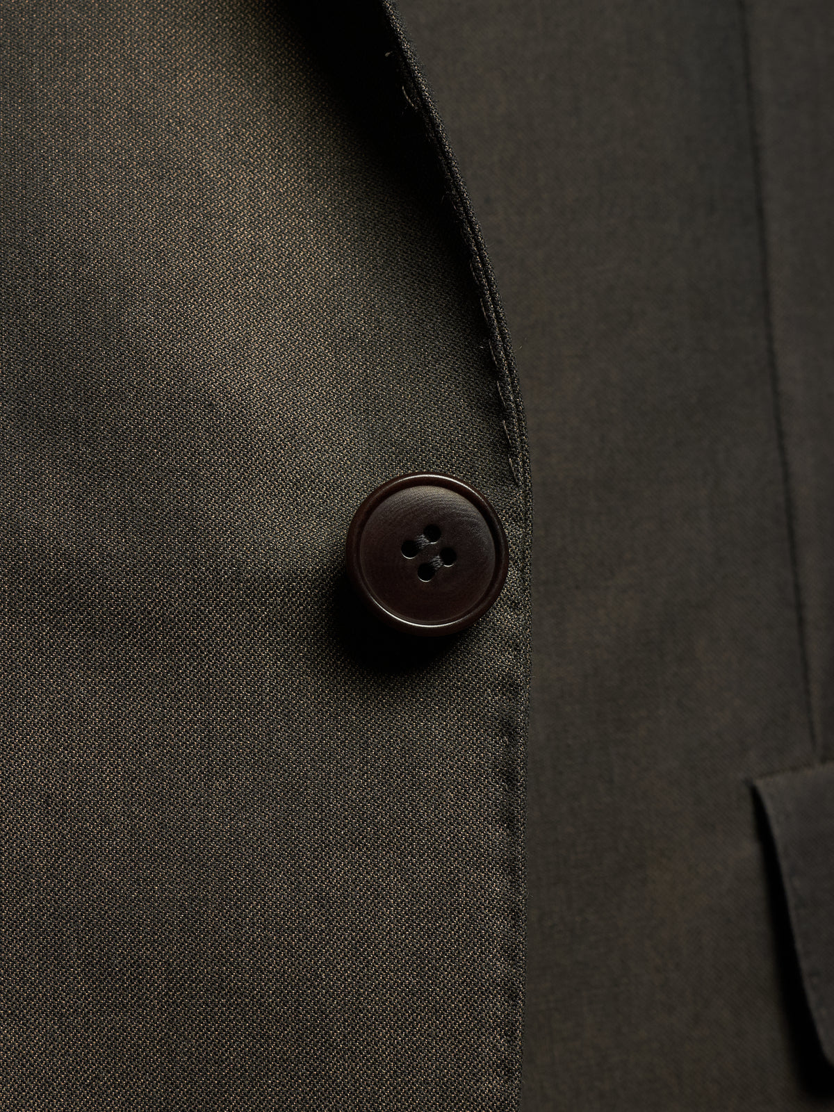Close-up detail of a dark olive-brown suit jacket showing the texture of the fabric and a single dark brown button.