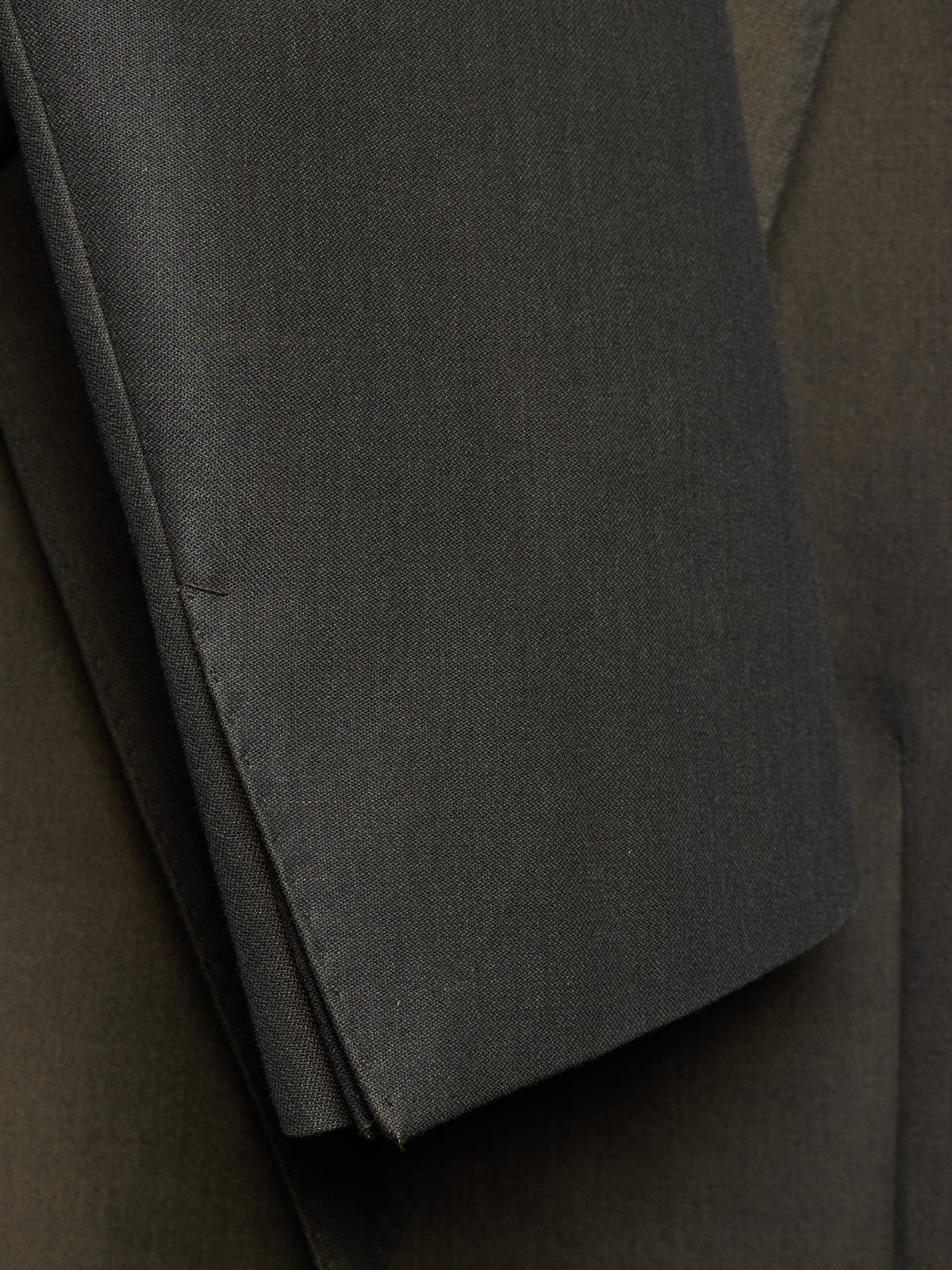 Close-up of a dark charcoal gray fabric sleeve or folded garment detail, showing the texture and stitching against a matching dark background.