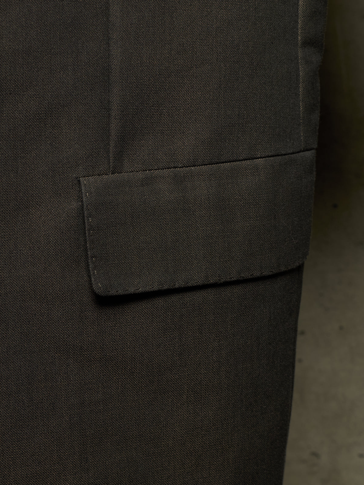 Close-up detail of a dark charcoal gray fabric garment, showing a pocket flap and textured woven material.