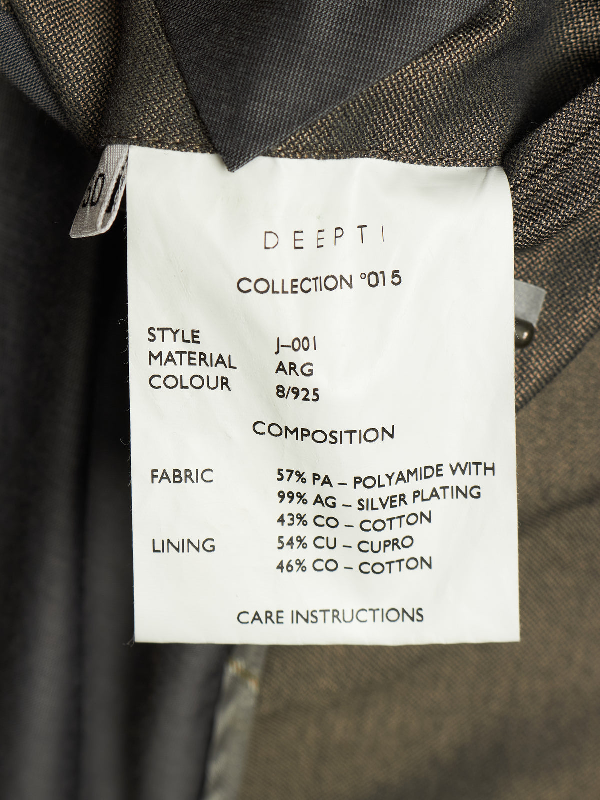 A close-up of a garment's inner collar showing a white paper label with printed specifications for 'DEEPTI COLLECTION °015'. The label details the style J-001, material ARG 8/925, fabric composition with 57% PA, 99% silver plating, 43% cotton, 54% copper, and 46% cotton.