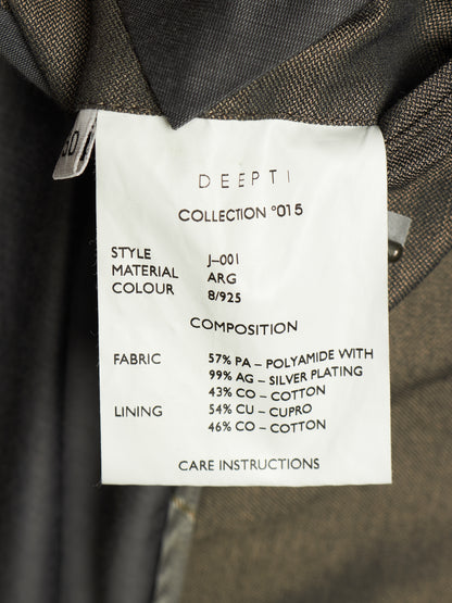 A close-up of a garment's inner collar showing a white paper label with printed specifications for 'DEEPTI COLLECTION °015'. The label details the style J-001, material ARG 8/925, fabric composition with 57% PA, 99% silver plating, 43% cotton, 54% copper, and 46% cotton.