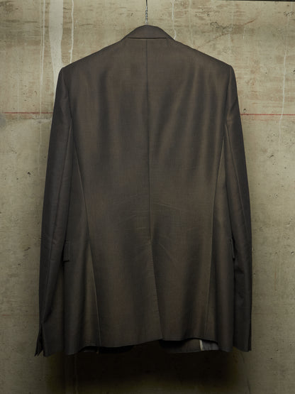 A dark brown tailored suit jacket hanging on a hanger against a textured concrete wall, showing the back view.