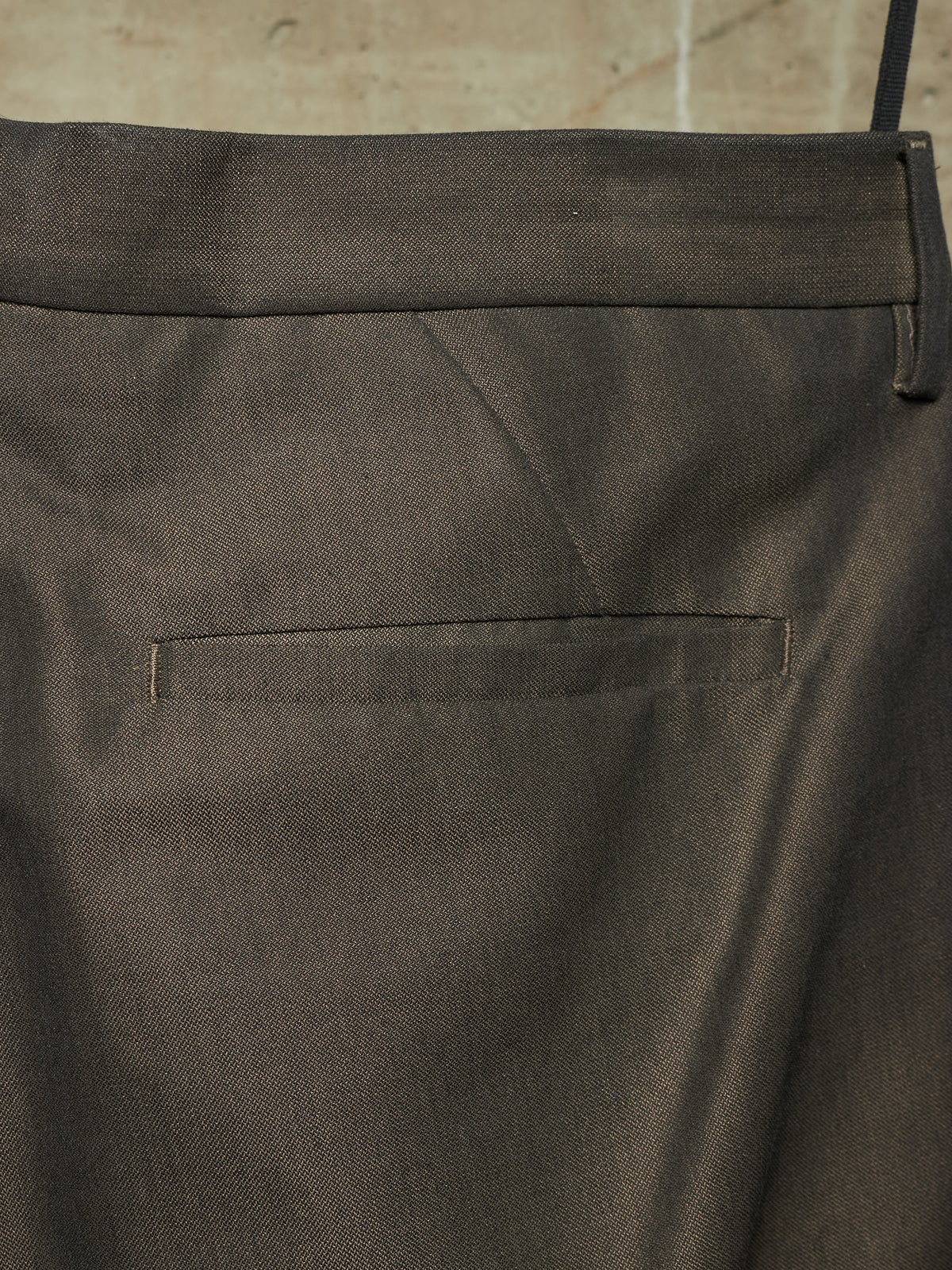 Close-up of the back waistband and pocket of dark charcoal gray trousers, showing the fabric texture and stitching.
