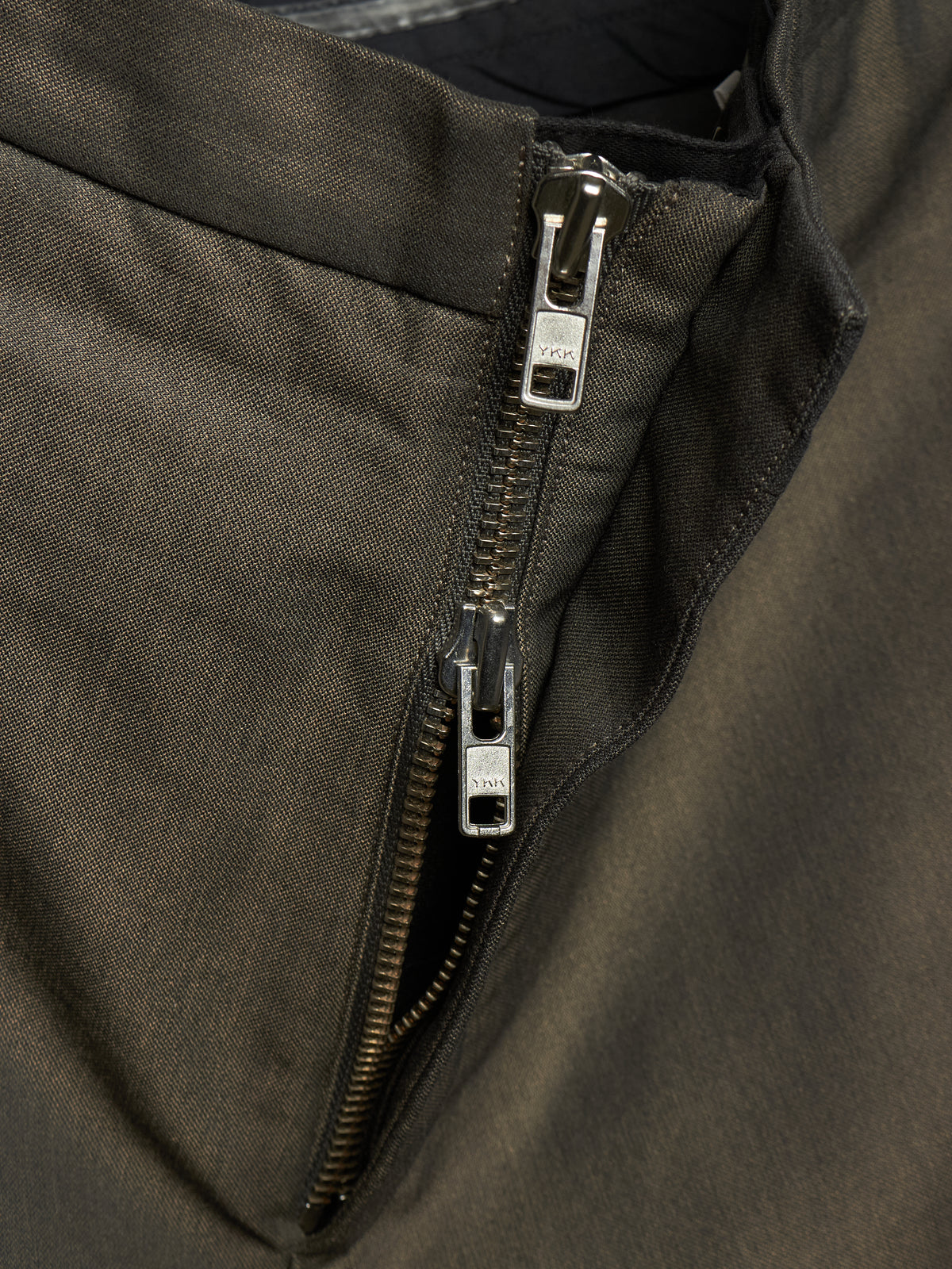 Close-up of a dark olive green jacket showing a silver metal zipper with a pull tab.