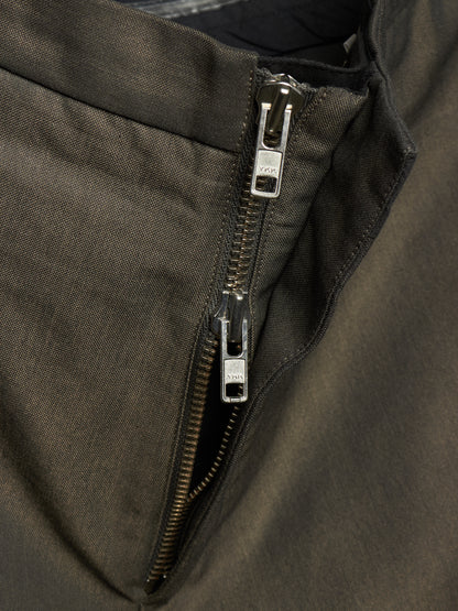 Close-up of a dark olive green jacket showing a silver metal zipper with a pull tab.