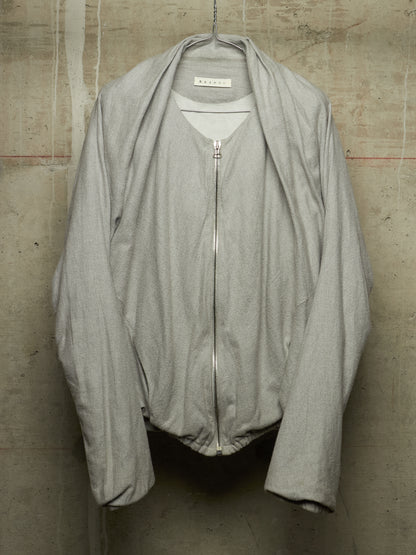 A light gray zip-up jacket with a wide collar and draped sleeves, hanging against a textured concrete wall. The brand label inside the collar reads 'M'ARMOUR'.