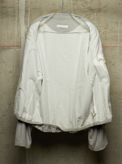 A white lightweight jacket with a wide collar and gathered elastic hem, hanging on a wire hanger against a textured concrete wall.