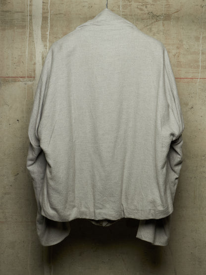 A light gray linen shirt jacket hanging against a textured concrete wall, showing the back view.