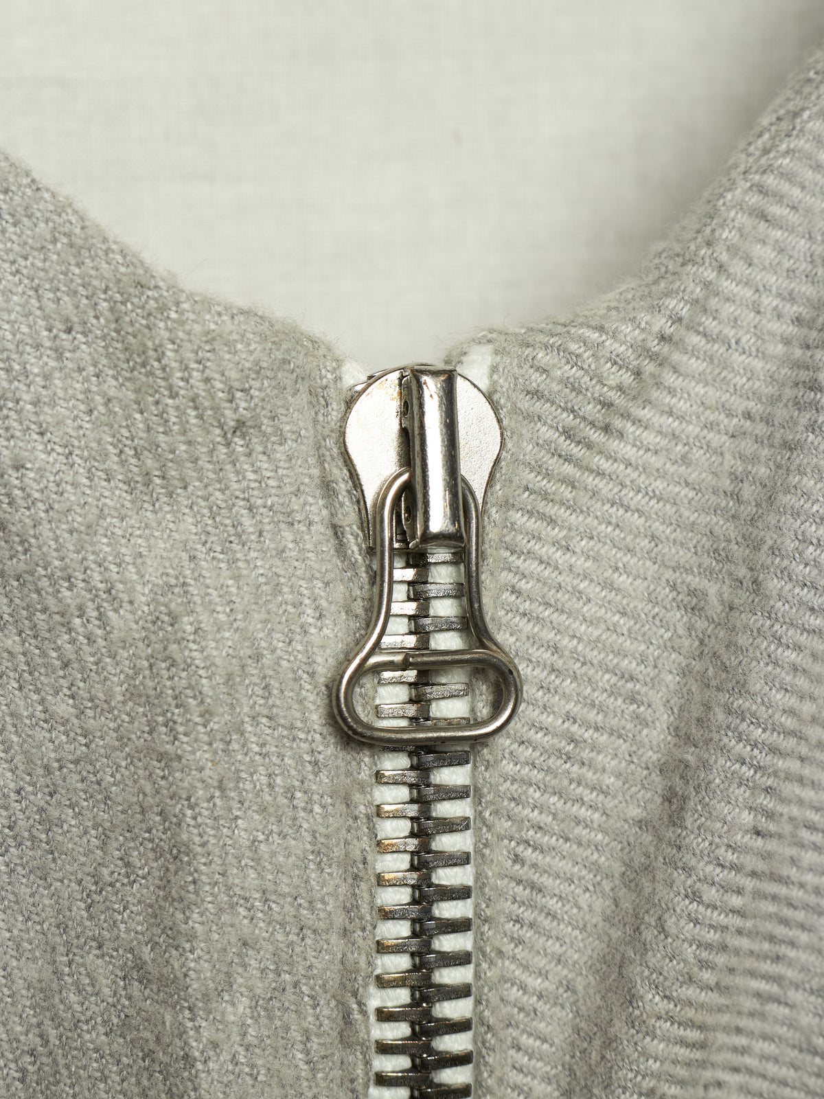 Close-up of a silver metal zipper pull on a light gray ribbed knit garment.