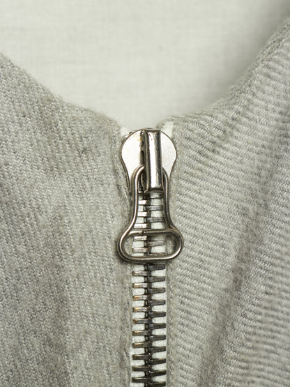 Close-up of a silver metal zipper pull on a light gray ribbed knit garment.
