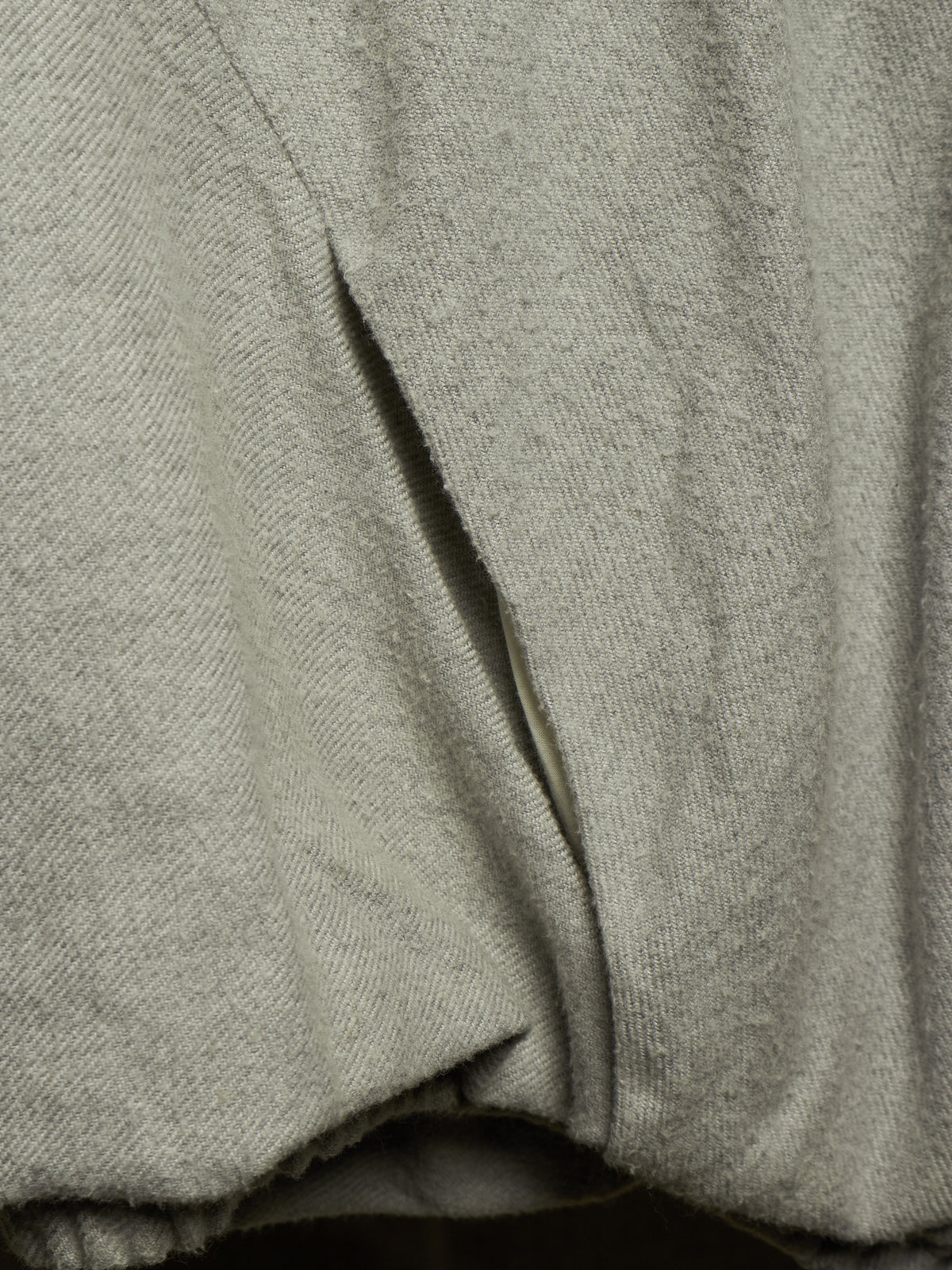 Close-up of a light gray knit fabric garment with a diagonal seam and soft draped folds.