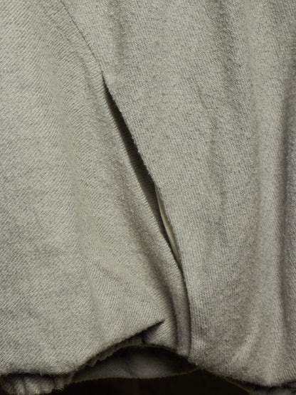 Close-up of a light gray knit fabric garment with a diagonal seam and soft draped folds.