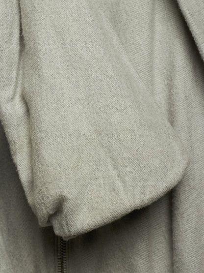 Close-up of a light gray textured fabric garment, showing a soft draped sleeve or cuff with a zipper detail at the bottom.