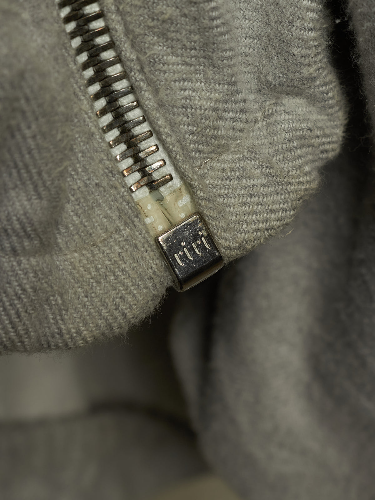 Close-up of a gray textured fabric zipper with a square metal pull tab engraved with the brand name 'cct'.