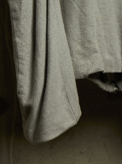Close-up of a light gray textured fabric garment, showing a folded cuff or hem with a visible metal zipper pull against a dark background.