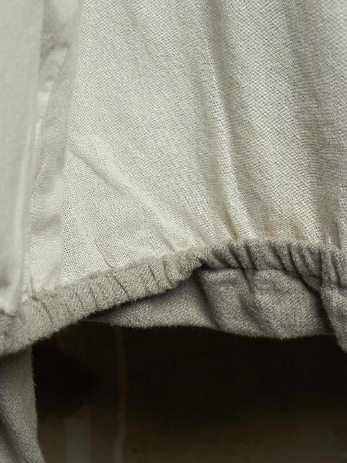 Close-up detail of a light beige or off-white fabric garment with a gathered elastic hem.