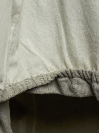 Close-up detail of a light beige or off-white fabric garment with a gathered elastic hem.