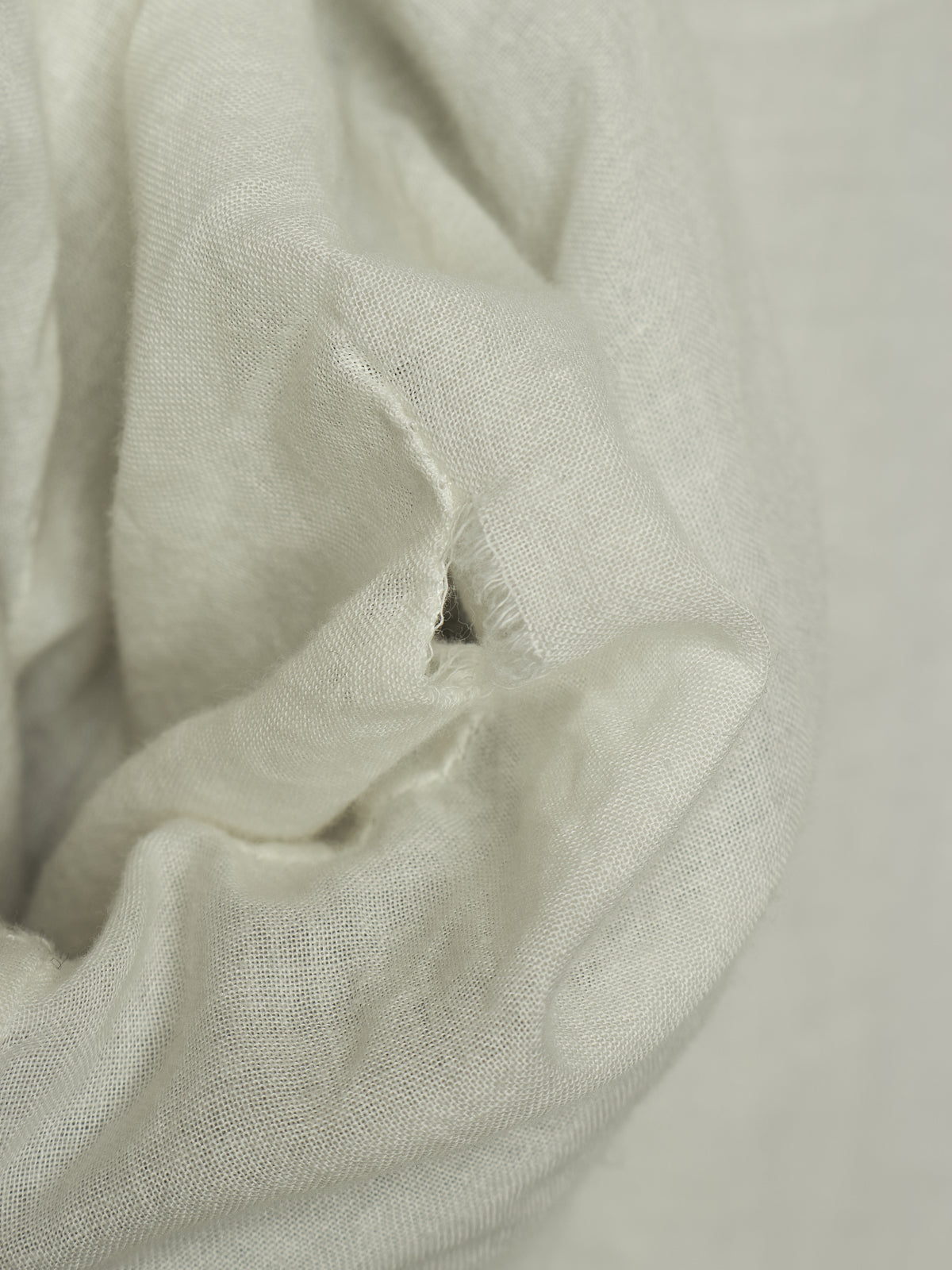 A close-up of draped off-white or cream-colored fabric with a visible small hole in the material.