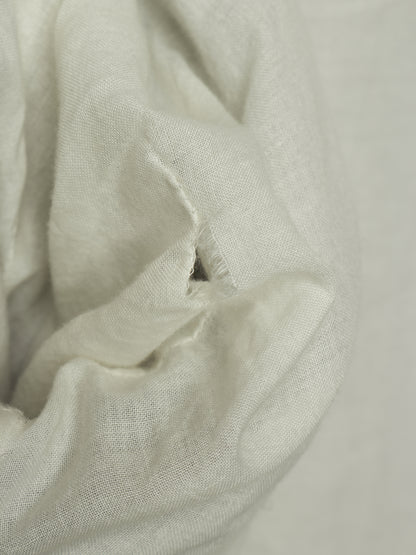 A close-up of draped off-white or cream-colored fabric with a visible small hole in the material.