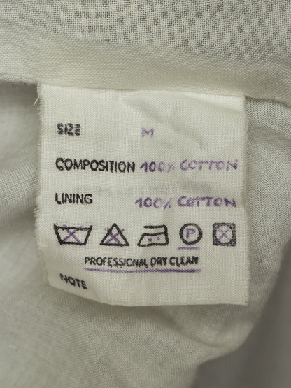 Close-up of a white fabric garment label showing size M, 100% cotton composition and lining, with care symbols and 'Professional Dry Clean' text.
