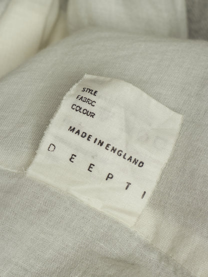 Close-up of a light beige fabric garment with a white sewn-in label reading 'DEEPTI MADE IN ENGLAND' and 'STYLE FABRIC COLOUR'.