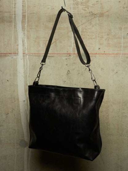 A black leather shoulder bag hanging against a textured concrete wall.