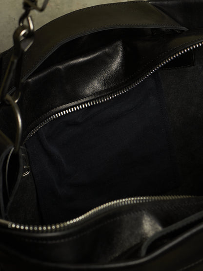 Close-up of the interior of a black leather bag, showing a dark fabric lining, silver zipper tracks, and part of a metal chain strap.