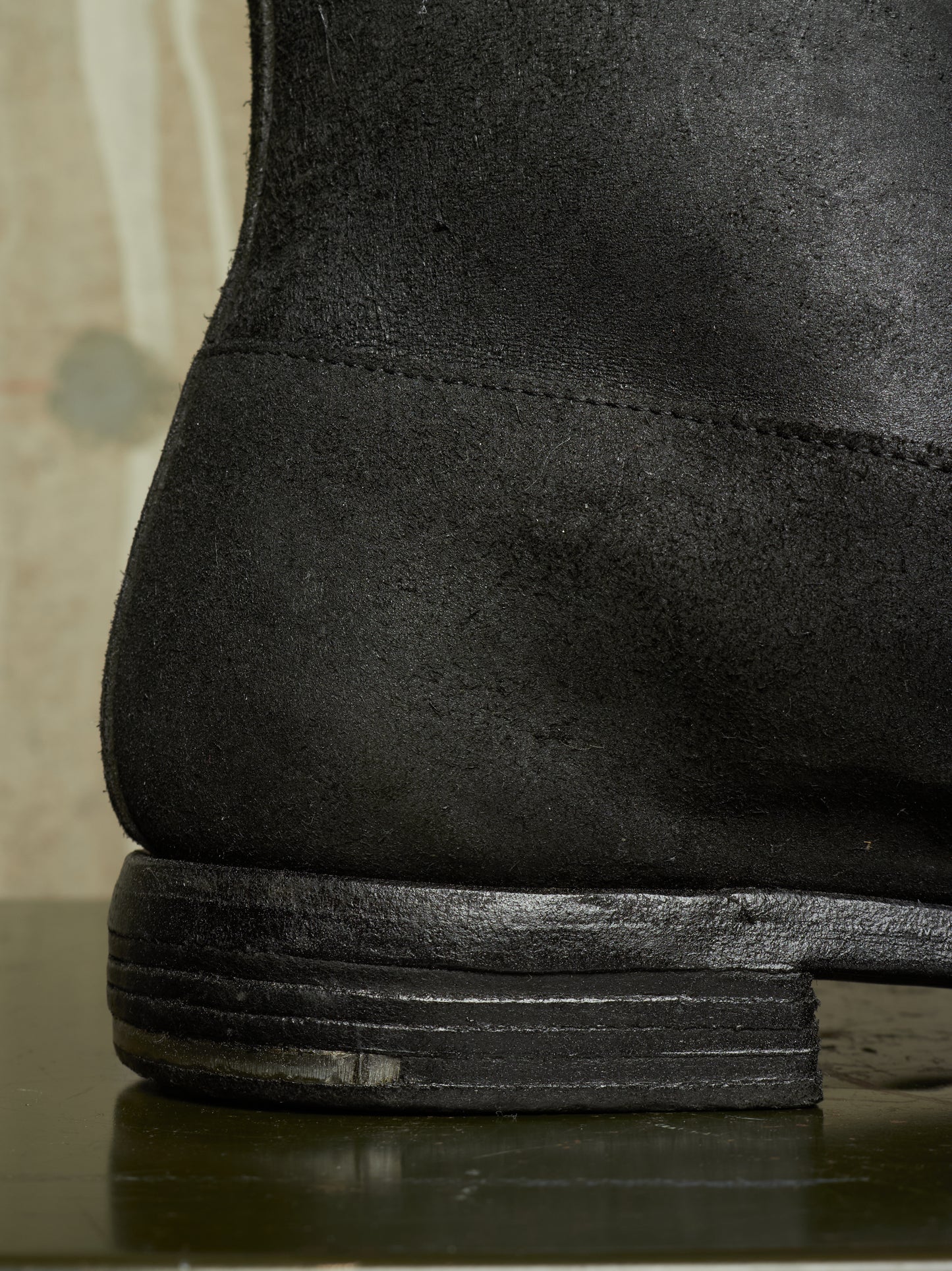 Close-up detail shot of the heel and stacked sole of a black suede boot.