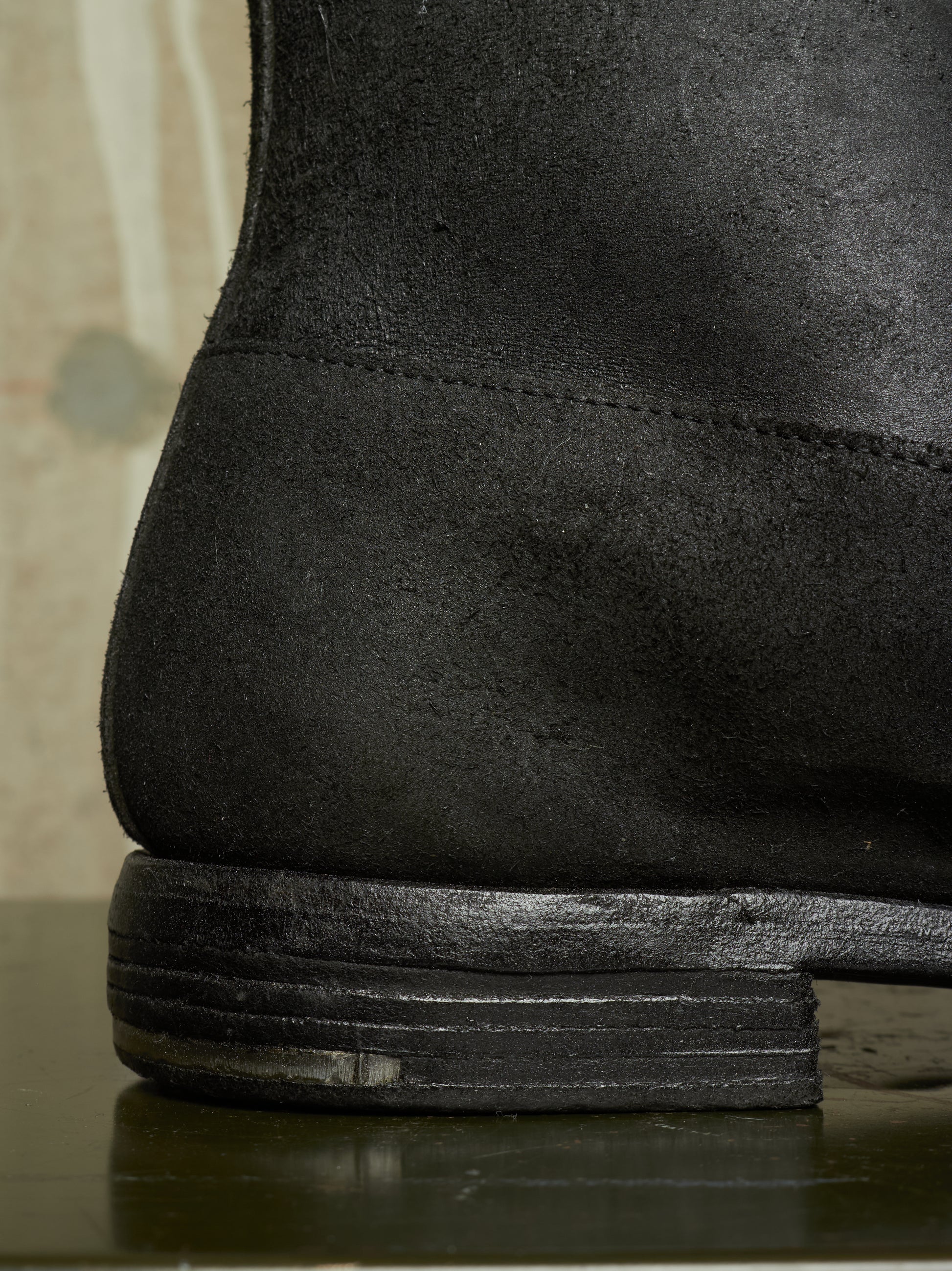 Close-up detail shot of the heel and stacked sole of a black suede boot.
