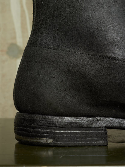 Close-up detail shot of the heel and stacked sole of a black suede boot.