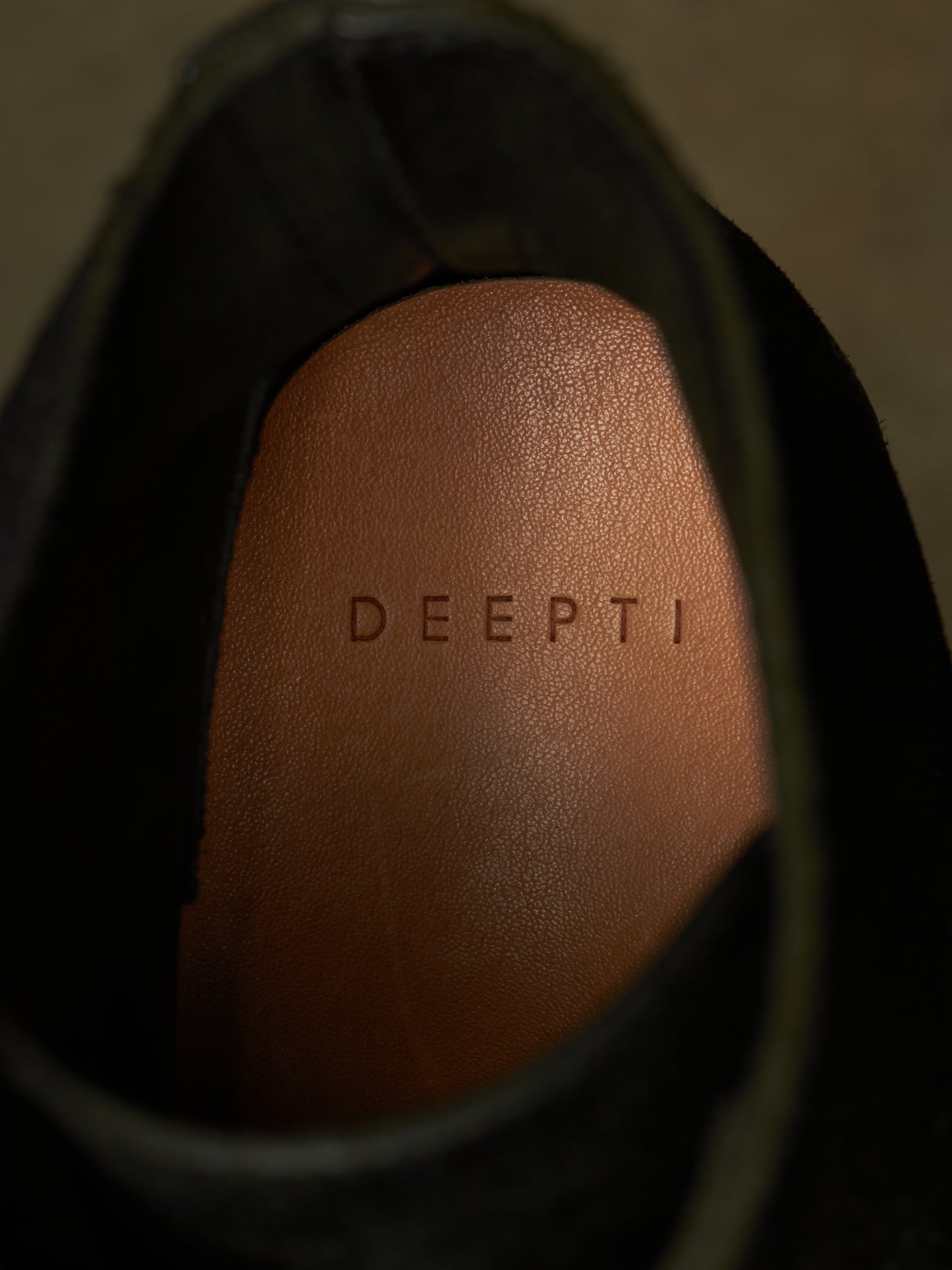 Close-up of the interior insole of a black shoe, showing the brand name 'DEEPTI' embossed on a tan leather footbed.