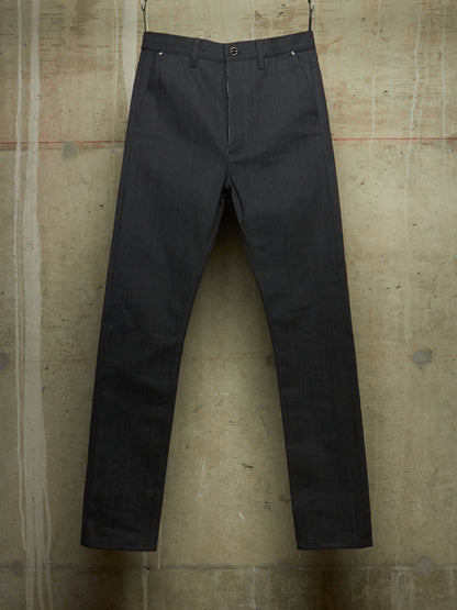 Dark charcoal gray slim-fit trousers hanging against a textured concrete wall.