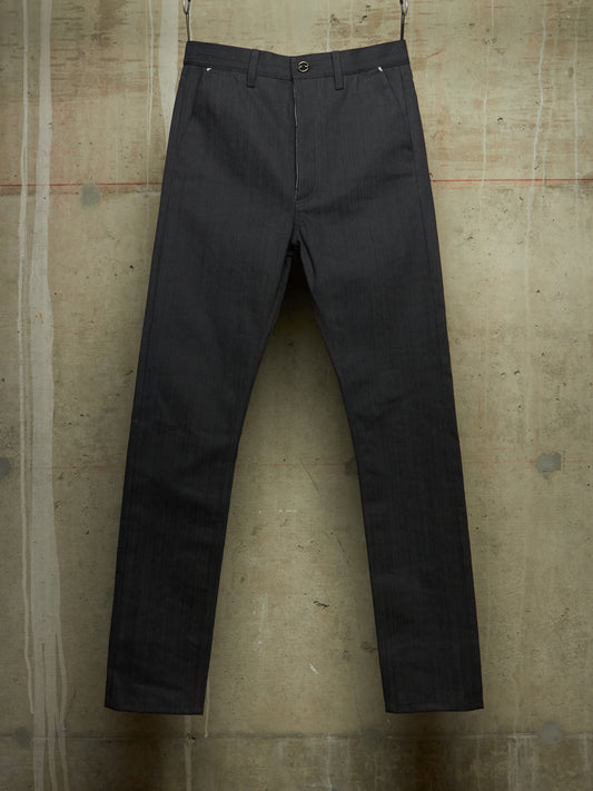 Dark charcoal gray slim-fit trousers hanging against a textured concrete wall.