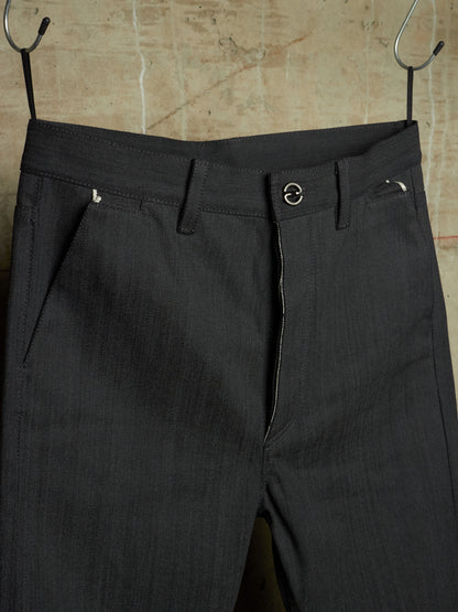 Dark charcoal gray pinstriped trousers hanging from black metal hangers against a textured beige wall.