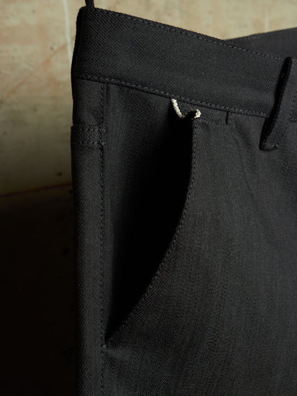 Close-up detail of black trousers showing the waistband, belt loop, and side pocket stitching.