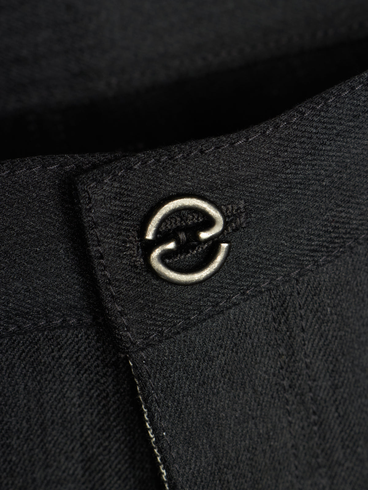 Close-up of a black textured fabric garment featuring a silver metal double-ring hardware detail on a stitched tab.