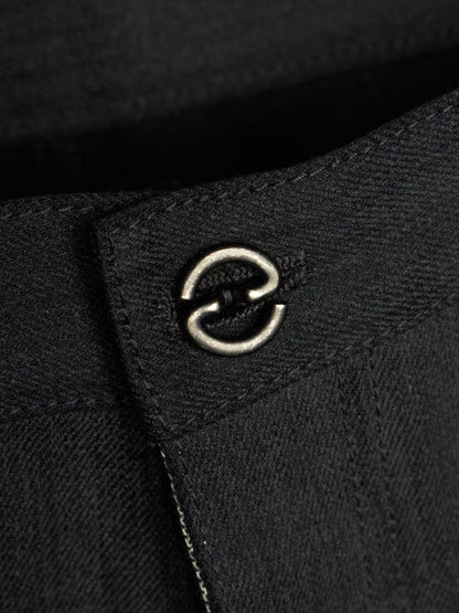 Close-up of a black textured fabric garment featuring a silver metal double-ring hardware detail on a stitched tab.