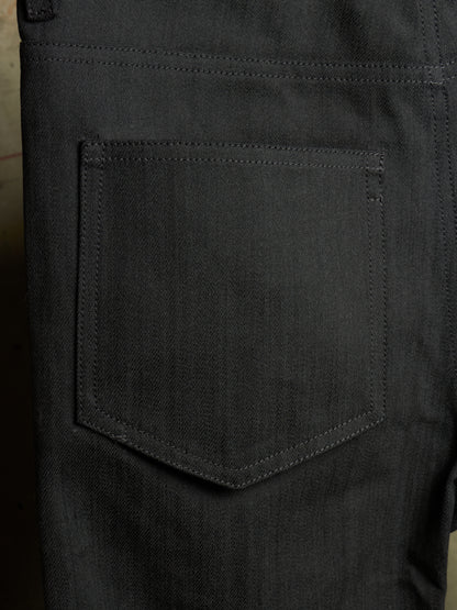 Close-up of the back pocket of dark charcoal gray denim jeans, showing the detailed fabric texture and stitching.