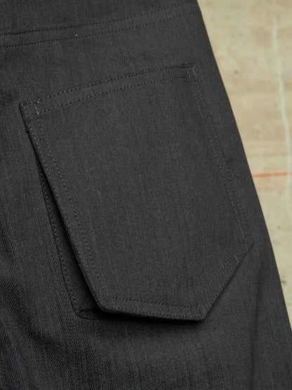 Close-up of the back pocket of dark charcoal gray denim jeans, showing the texture of the fabric and precise stitching.