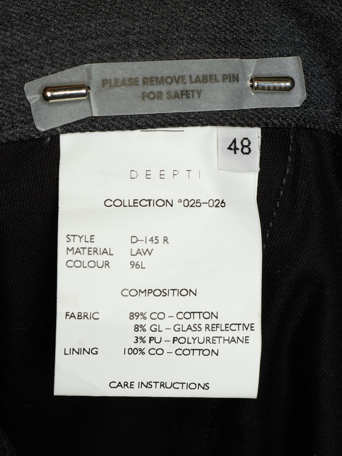 Close-up of a garment interior label reading DDEPTI, with size 48 and fabric details on a black fabric background.