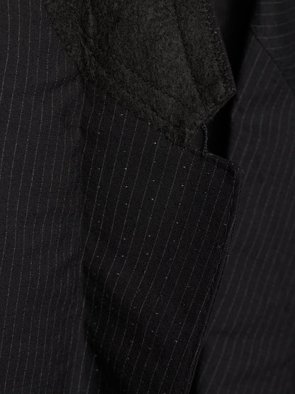 Close-up of a black pinstripe suit jacket showing the textured fabric, fine vertical stripes, and a dark charcoal fuzzy lapel detail.