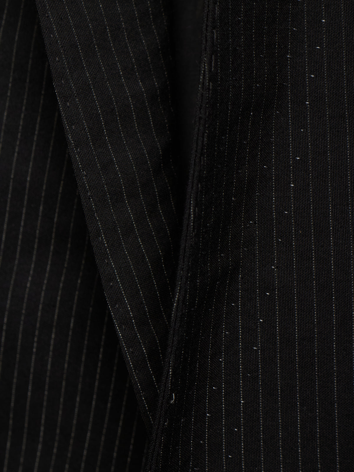 Close-up of a black pinstripe fabric, showing fine vertical white stripes and subtle shimmering details.