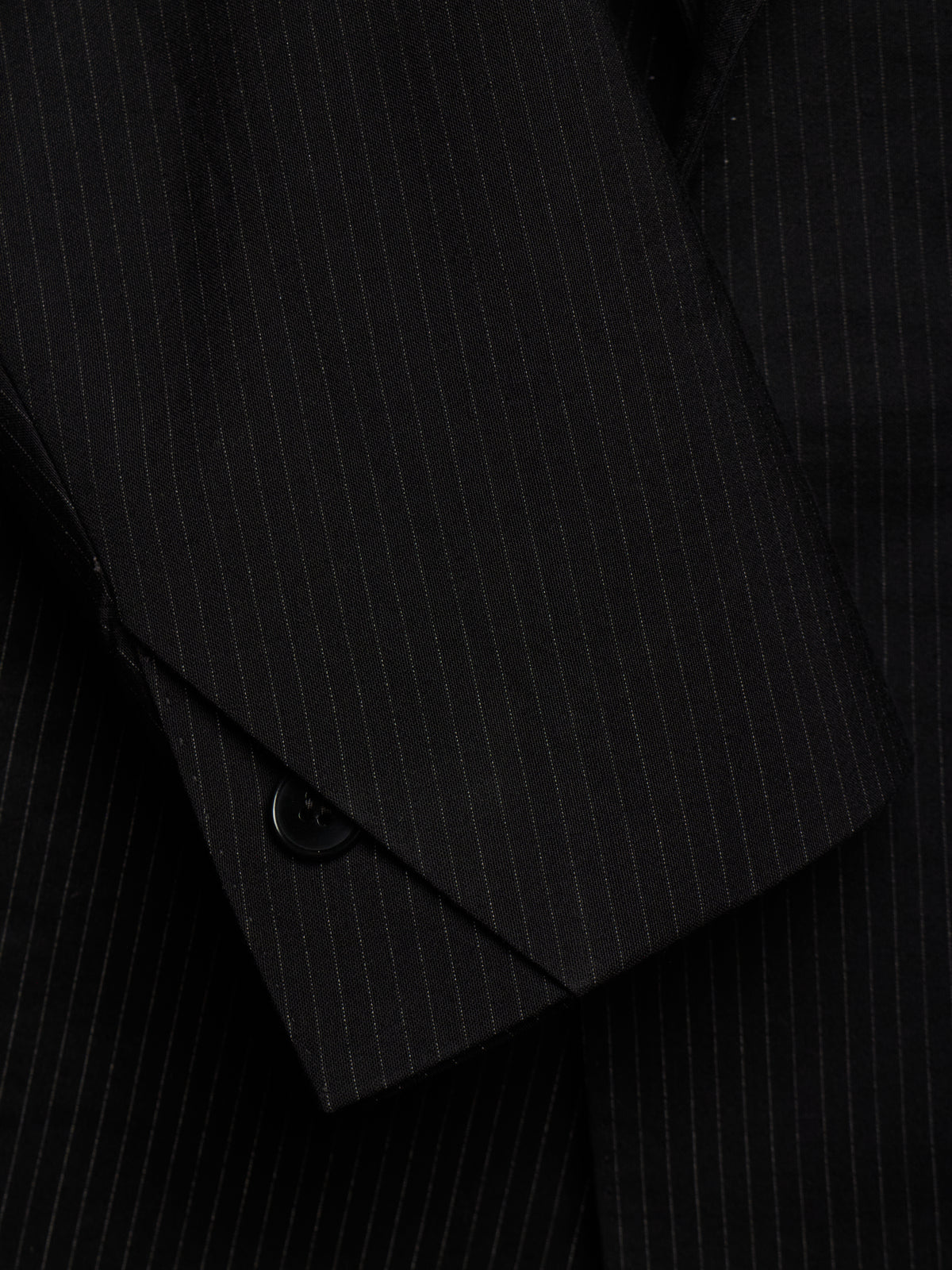 Close-up of a black pinstriped suit jacket, showing the fabric texture and a buttoned cuff detail.