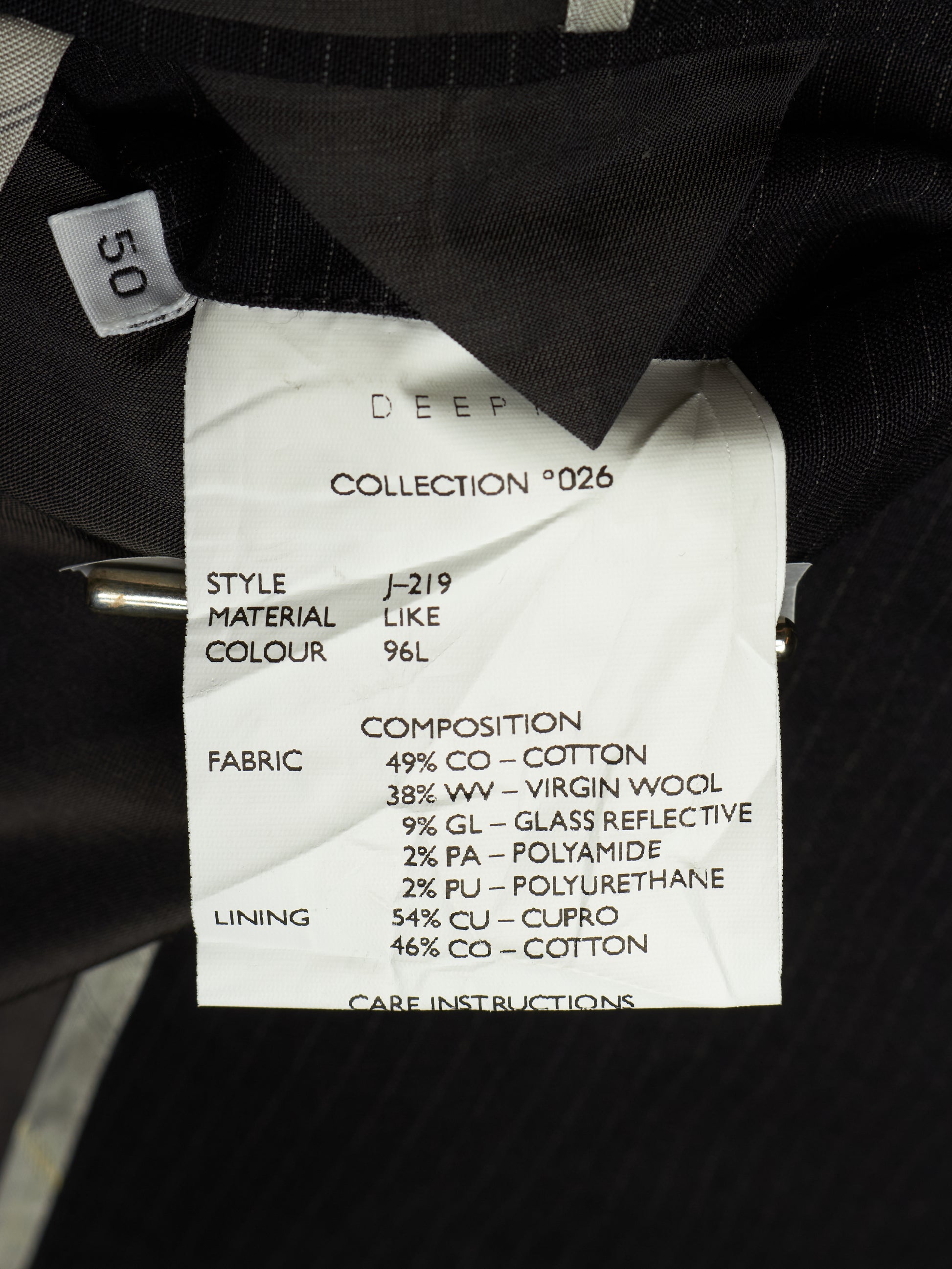 Close-up of a garment's interior label showing details such as style J-219, material composition, and fabric details, with a small size tag reading 50.
